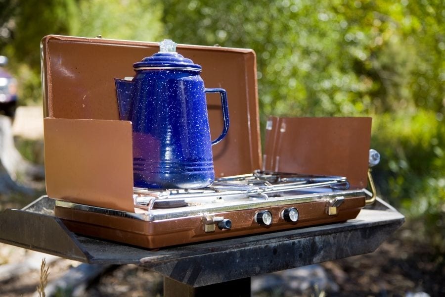 A blue hot water kettle sits on a brass colored camp stove