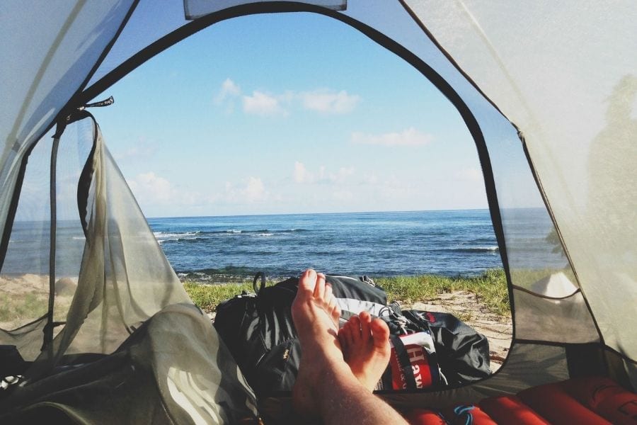 A camper lays in their tent facing out towards the ocean