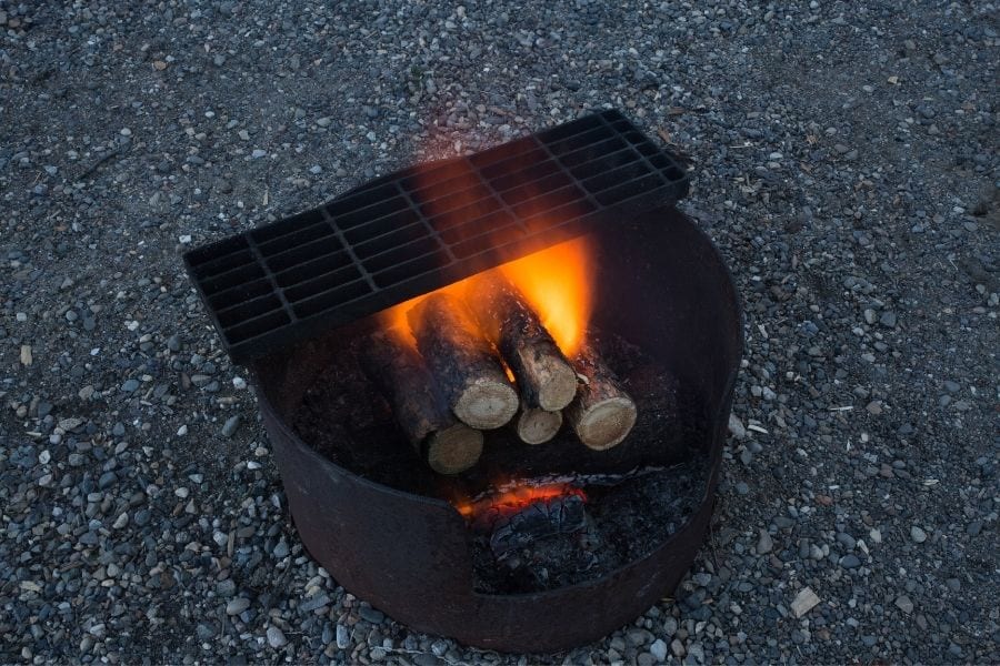 A wood fire burns in a campfire pit and grill in a campground