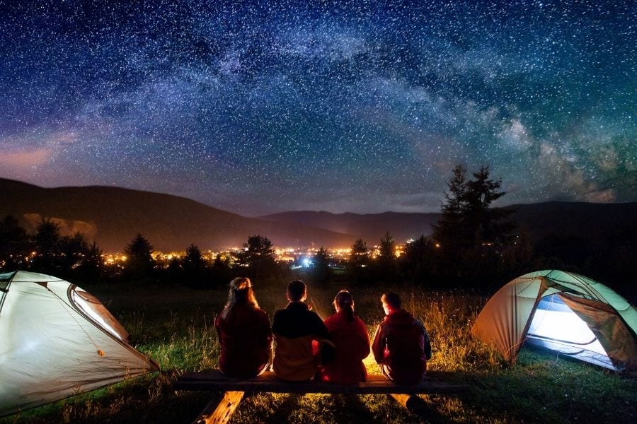 Four friends watch the stars in the nightsky at their campsite near a city